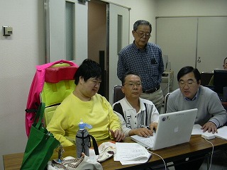 講師が受講者のパソコンを操作しているところをみんなで覗いている様子の写真
